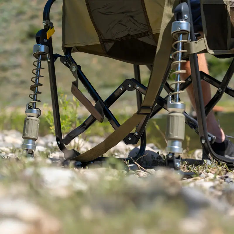 Close-up of the suspension legs on a tan Adjustable Rocker set on uneven, rocky ground.
