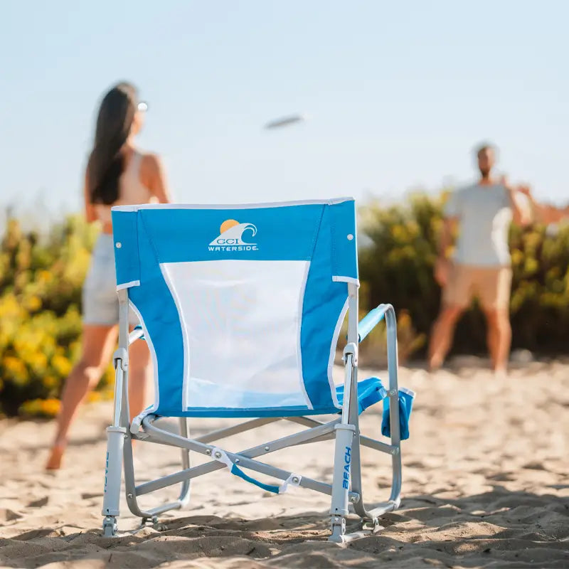 Back view of Saybrook Blue Beach Rocker showing mesh panel and GCI Waterside logo as people play frisbee in the background.