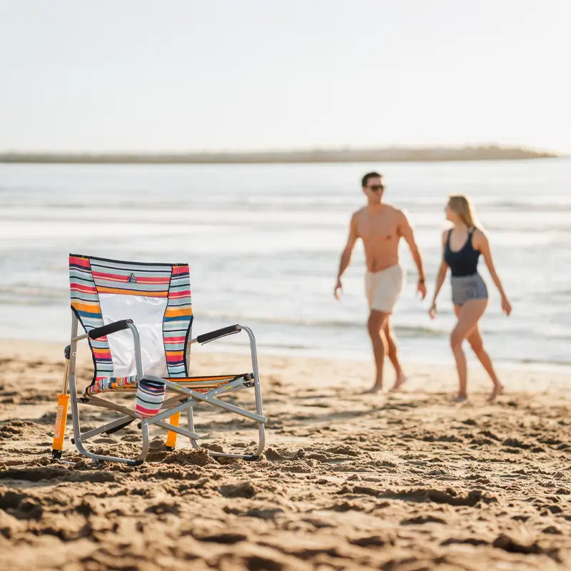 Striped Beach Rocker Chair sitting on the beach, with two people walking in the background.