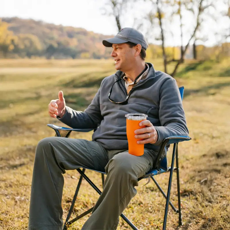 Man sitting in a heathered royal Comfort Pro Chair, chatting and holding an orange drink.