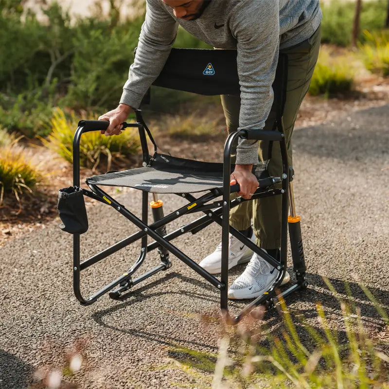Man sets up a Black Freestyle Rocker Elite chair on a sunlit walking path.