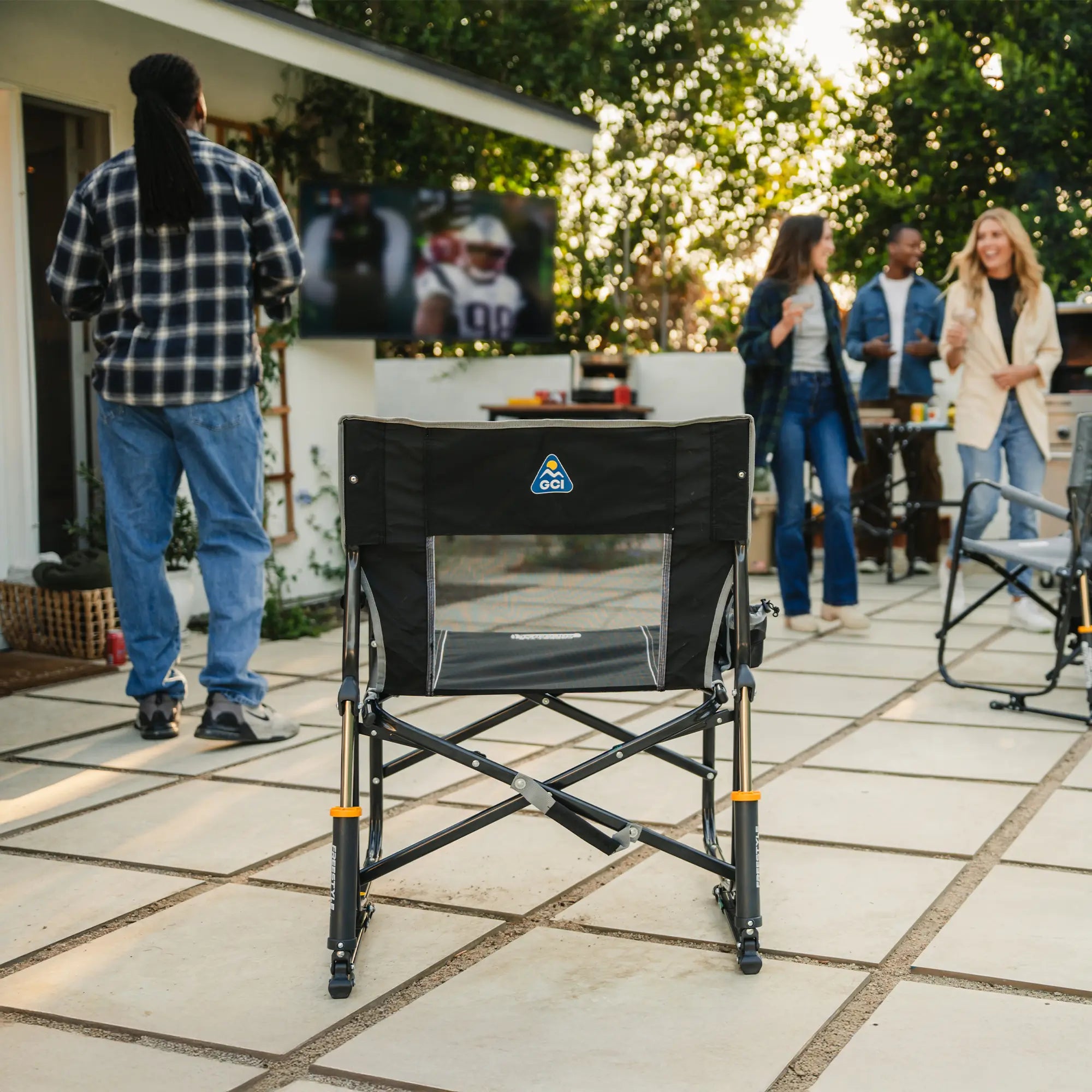 A black freestyle rocker standing in the middle of a group of people who are watching a football game on television.