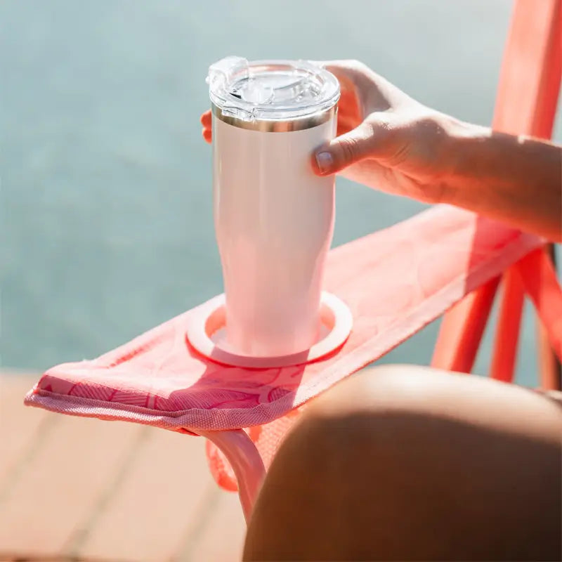 Hand places a tumbler into the cupholder of a Soft Pink Leaf Kickback Rocker by the pool.