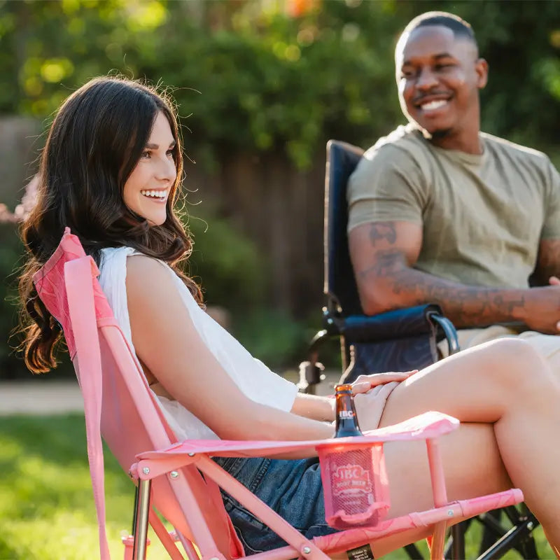 Woman relaxes and smiles in a Soft Pink Leaf Kickback Rocker while chatting in a backyard.