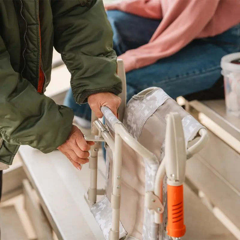 Hands adjust l-hook lever on the Snow Camo Stadium Rock-Cliner in stadium bleachers.