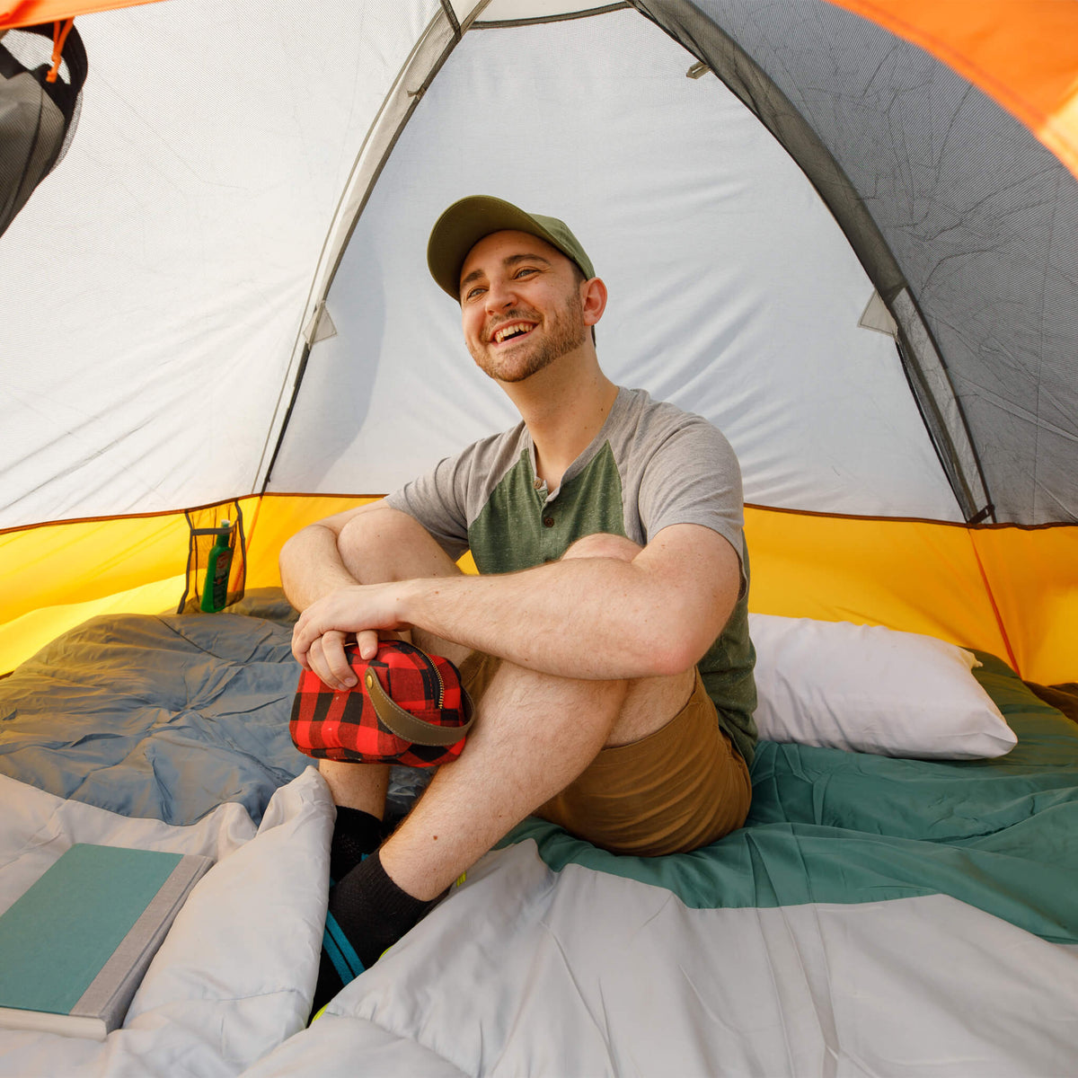 Camper relaxing inside CORE 3 person dome tent with mesh ceiling and bright interior, seated on sleeping bag with gear.