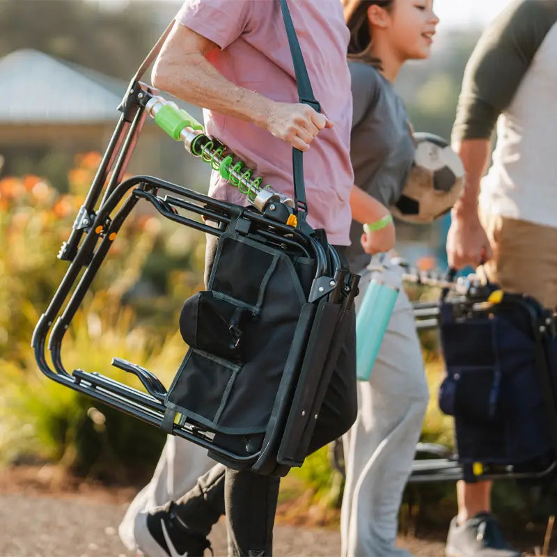 Person carries a folded black Adjustable Rocker over their shoulder, walking with others holding sports gear.