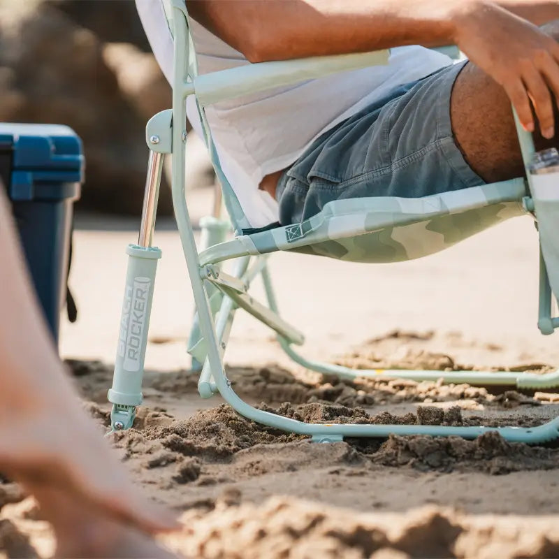 Close-up of the Green Beach Wave beach rocker’s leg and frame resting in soft sand.