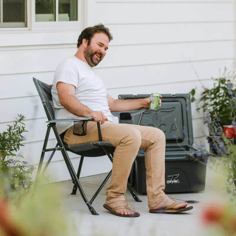 Man laughing while seated in a Comfort Pro Chair beside a cooler on a patio.