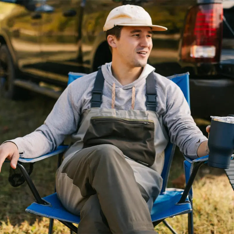 Man in waders sitting in a heathered royal Comfort Pro Chair, holding a navy tumbler.