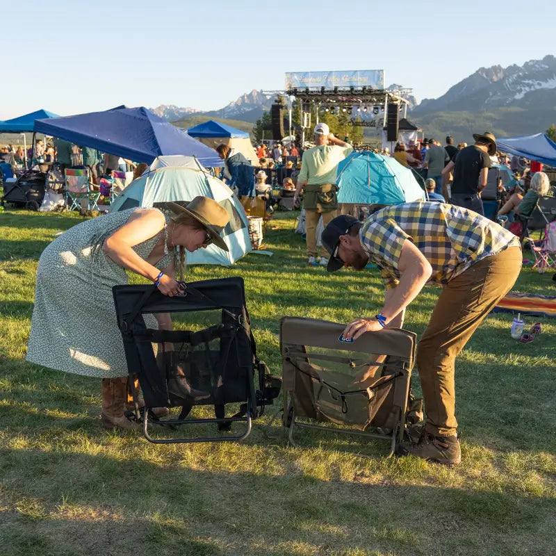 Man and woman folding aged fatigue and black Everywhere Chair 2s after an outdoor concert.
