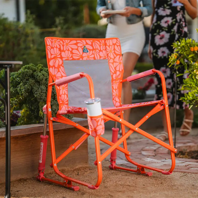 Freestyle Rocker in orange floral print sits near a garden bed with a tumbler in the drink holder.