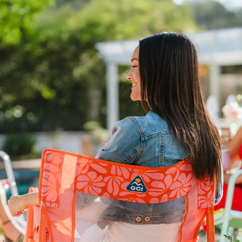 Close-up of the orange floral Freestyle Rocker’s mesh back and logo as a woman relaxes outdoors.