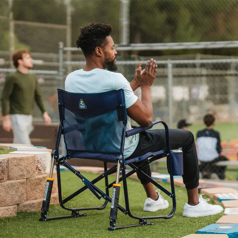 Man claps while seated in a Rich Blue Freestyle Rocker Elite chair at a baseball field.