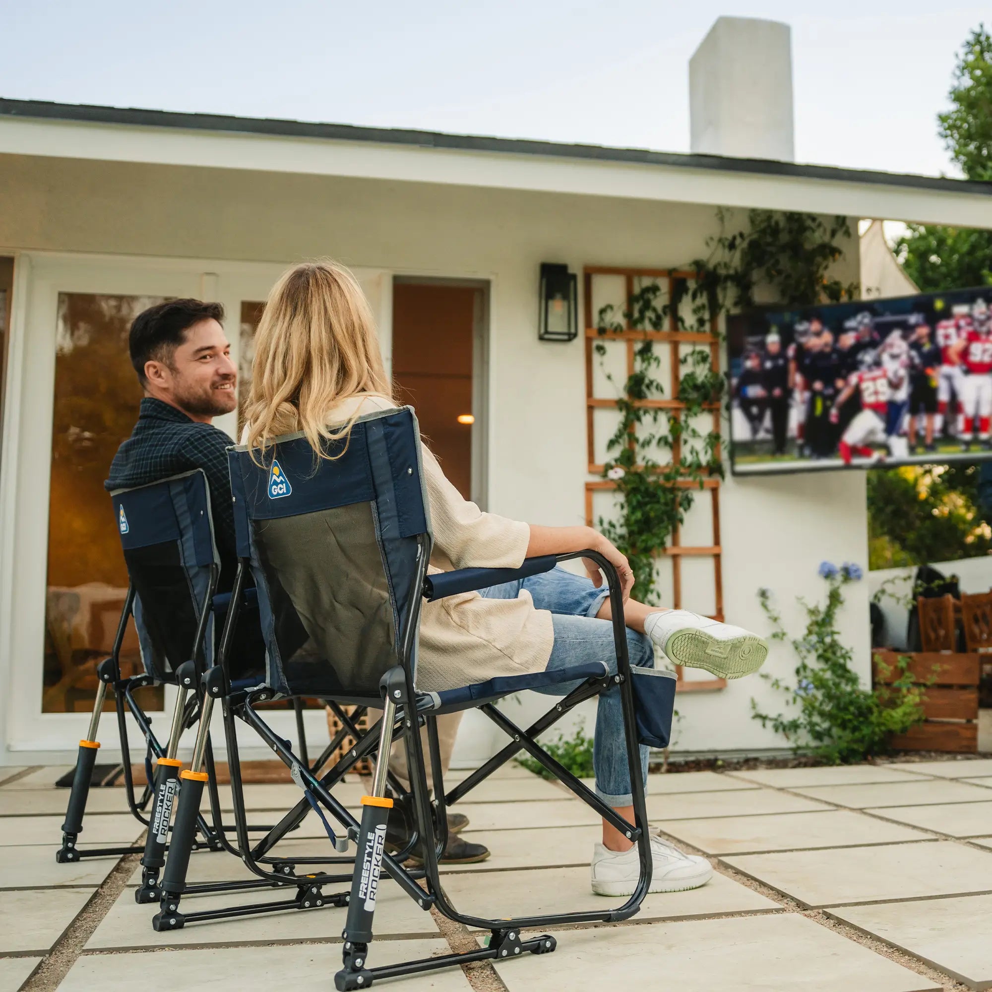 A couple sitting in two indigo freestyle rocker chairs while watching a football game on television. 