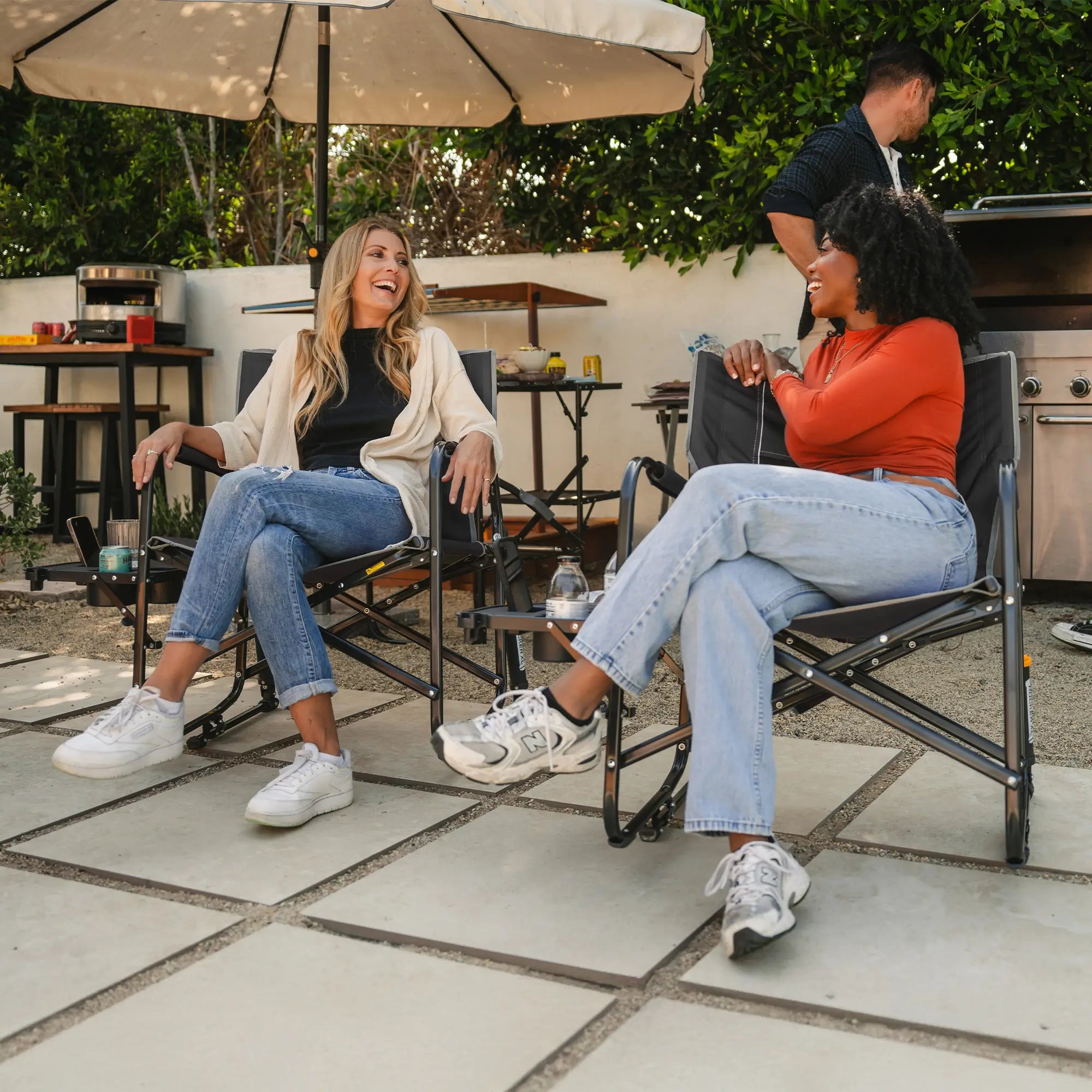 Two women conversing while sitting in their black freestyle rocker xl with side table on a patio. 