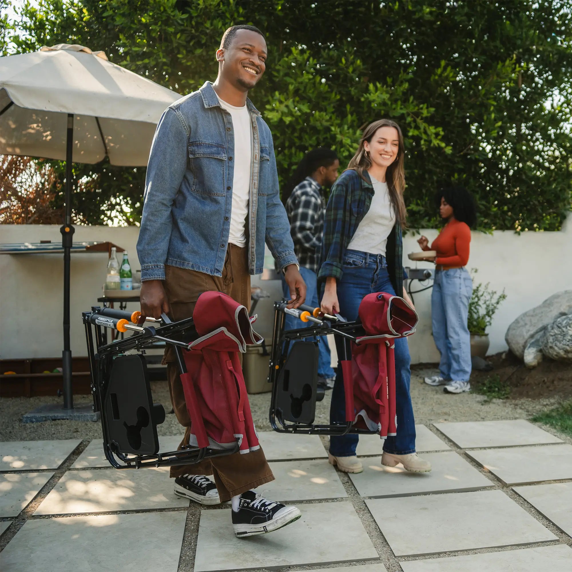 Two people carrying their red freestyle rocker xl with side table by using the integrated carry handle. 