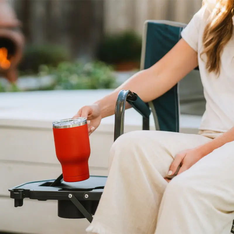 Woman placing a red tumbler in the built-in side table cup holder of the Freestyle Rocker.