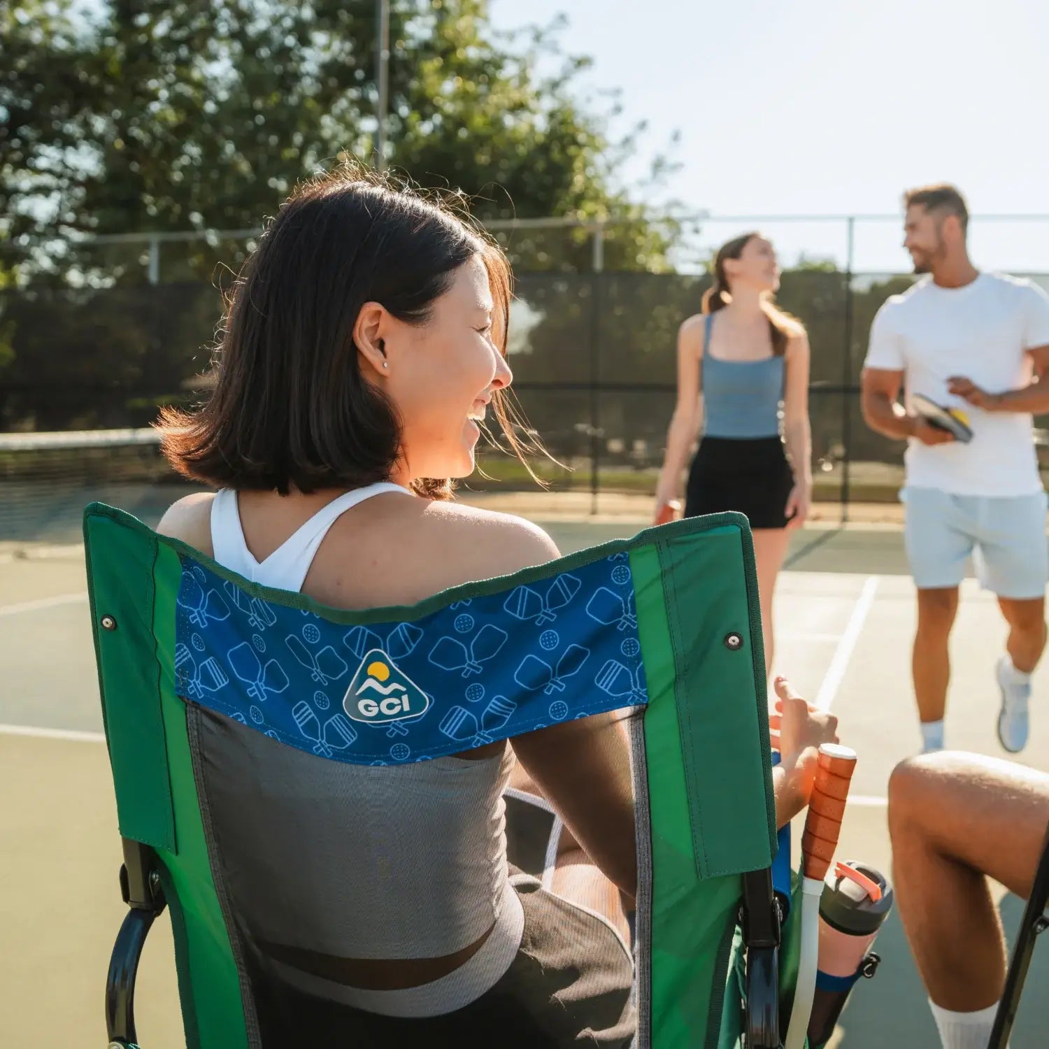 Woman laughing while sitting in pickleball stowaway rocker while people approach her. 