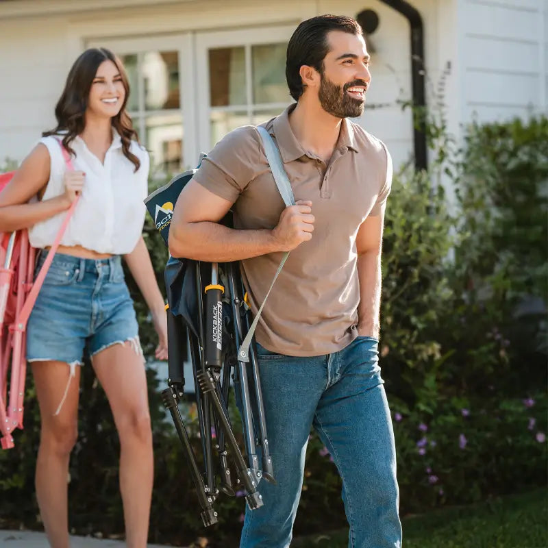 Man carrying the folded heathered indigo Kickback Rocker over his shoulder, smiling outdoors.