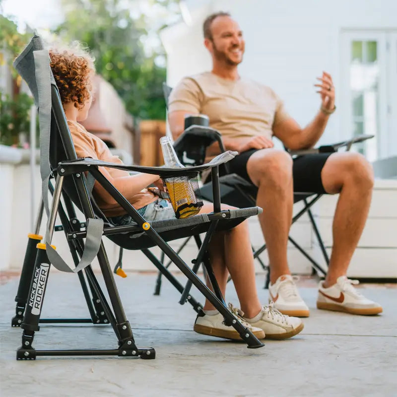 Young child and man chatting on a patio, with the child seated in a heathered pewter Kickback Rocker.