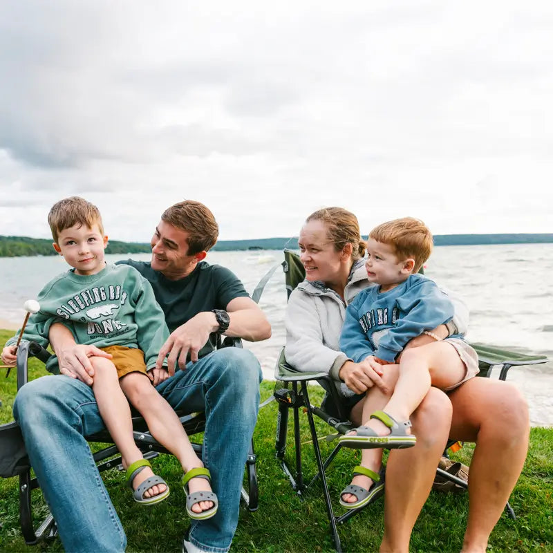 Family sitting by a lake on heathered loden Kickback Rockers, enjoying time together outdoors.