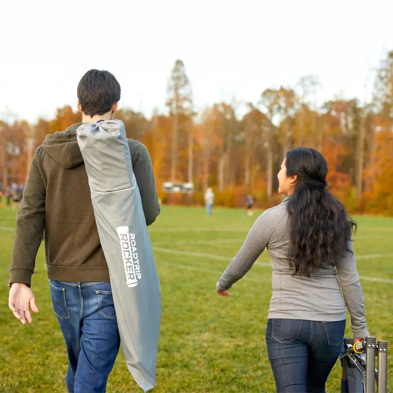 Couple walking across a field carrying Roadtrip Rocker chairs in carry bags.