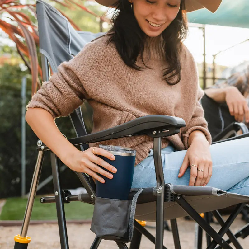 Woman places tumbler in mesh cupholder on mercury gray Roadtrip Rocker.