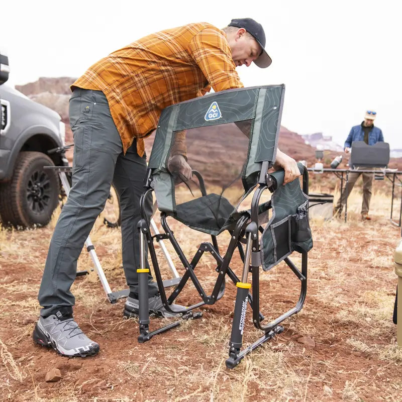 Man continuing to set up the hunter topo Stowaway Rocker outdoors near a truck and camping table.