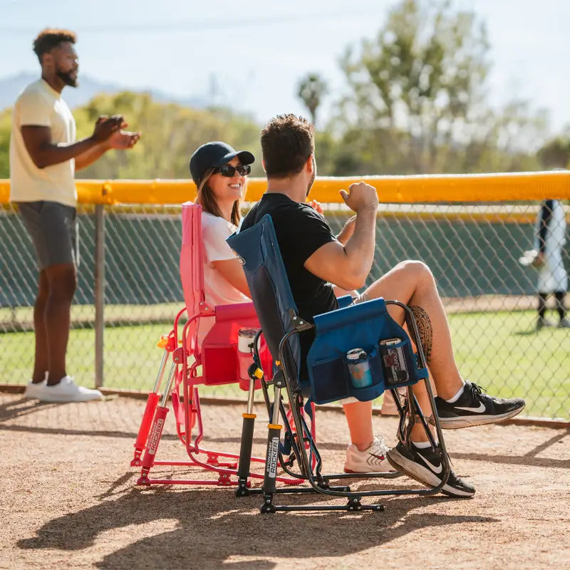 Man and woman seated in soft navy and pink Stowaway Rockers at a baseball field, cheering on players.