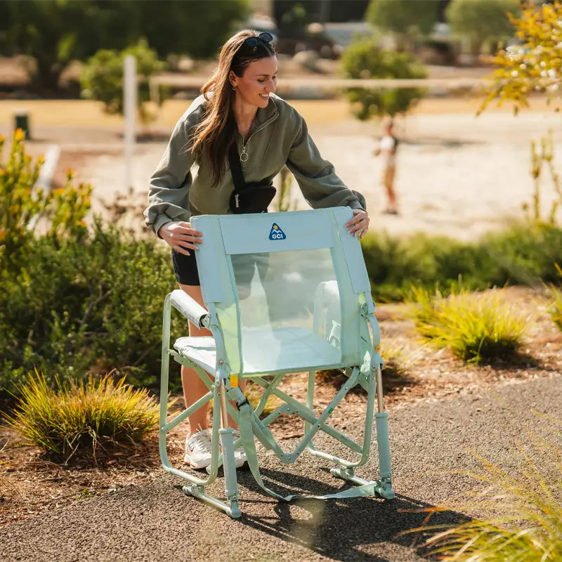 Woman setting up a pastel green Stowaway Rocker with a mesh backrest showing the GCI logo.